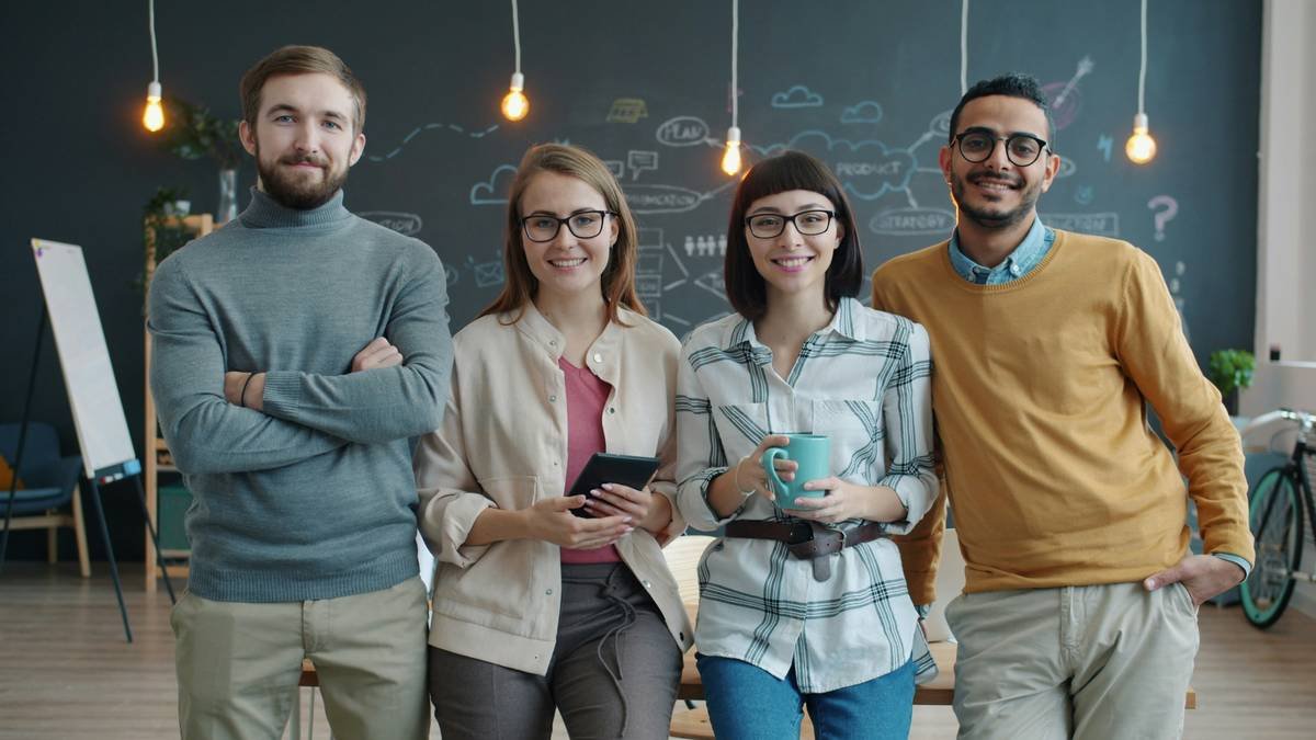 Portrait of cheerful young people coworkers standing in creative shared office smiling looking at camera. Multi-ethnic team and workplace concept.