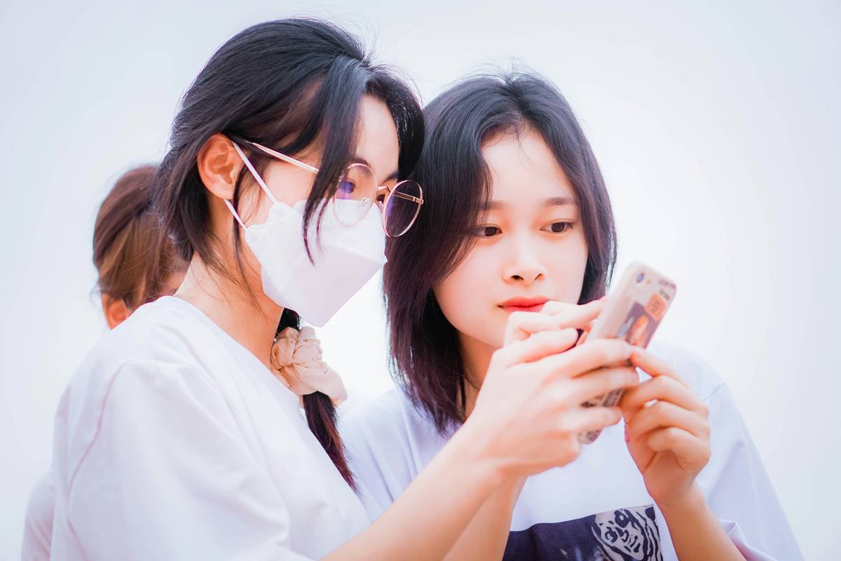 two asian women wearing face masks looking at a cell phone